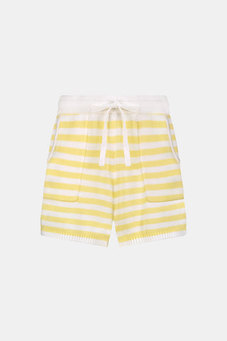 A person wears Roller Rabbit’s Striped Brie Short—a knit yellow and white horizontal striped short with a white drawstring at the elastic waistband and hands tucked in the front pockets.