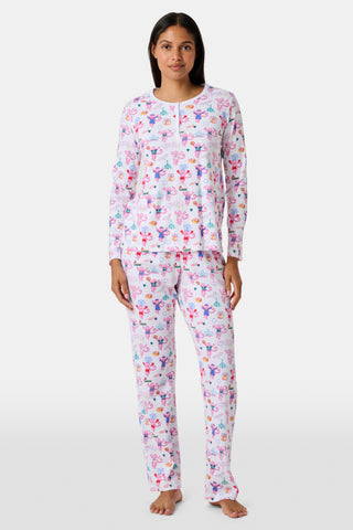 A woman stands barefoot wearing a matching long-sleeve Roller Rabbit Philly Monkey Pajamas set featuring a colorful floral and animal print on a white background.