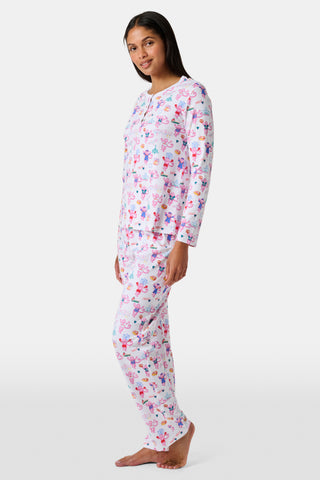 A woman stands barefoot wearing a matching long-sleeve Roller Rabbit Philly Monkey Pajamas set featuring a colorful floral and animal print on a white background.