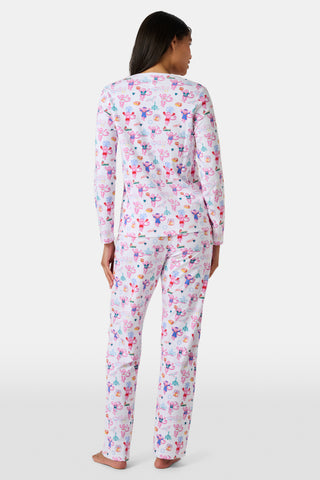 A woman stands barefoot wearing a matching long-sleeve Roller Rabbit Philly Monkey Pajamas set featuring a colorful floral and animal print on a white background.