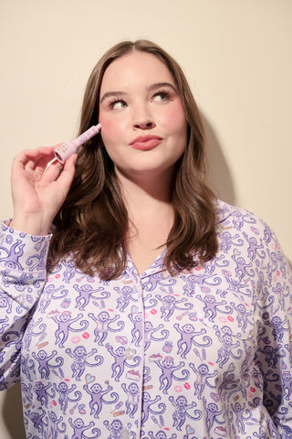 A woman smiles while wearing the TEXPIMA Get Ready With Me Blake Robe, featuring a knee-length cut and a purple and pink paisley pattern, tied at the waist, against a plain white background.