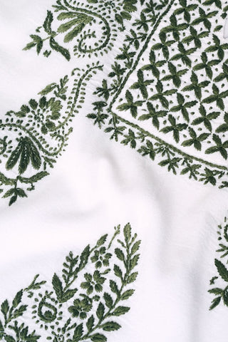 The Faith Top by Roller Rabbit is a white cotton blouse with green floral and geometric hand embroidery, including leaves, flowers, and a grid design. The textured base highlights the needlework. Made in India.