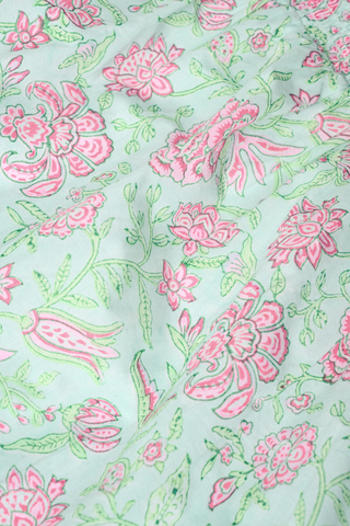 Close-up of light blue fabric on the Roller Rabbit Camellia Block Keaton Dress, showing hand-drawn floral and leaf motifs in a repeating pattern. This cotton summer dress features soft folds and a smooth texture.