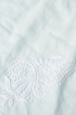 Close-up of the Faith Dress by Roller Rabbit, showcasing light blue fabric with delicate white hand-embroidered floral and paisley patterns for a subtle textured look.