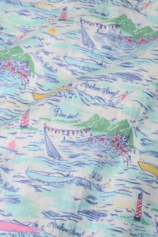A close-up of the Roller Rabbit Regatta Boyfriend Dress fabric, showing pastel sailboats, seaside houses, water, and playful phrases like “Sail Sail,” “Anchor Away,” and “Dine In!”.