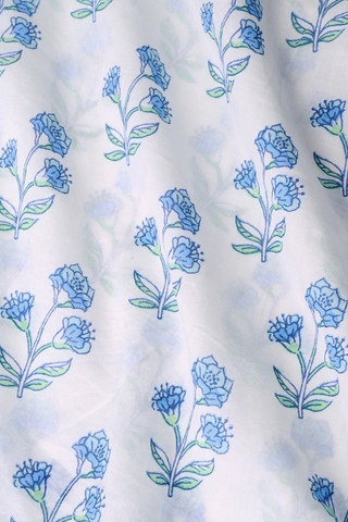 A woman with long dark hair wears the Roller Rabbit Rosa Floral Quincy Top, a cotton voile blouse with puffed sleeves, ruffled tie neckline, and matching blue flower patterns as part of a coordinating set.