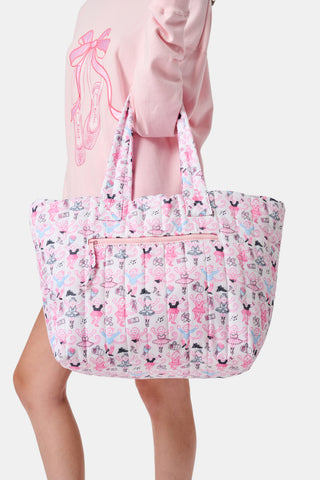 Wearing matching pink and white floral shorts and top, a person stands by lockers holding the Roller Rabbit Monkey Pirouette Quilted Tote, paired with white socks and blue sneakers.