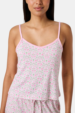The Garden Gate Floral Lily Set by Roller Rabbit features a pink and white women's loungewear set with a sleeveless, V-neck camisole and loose pants. Made from soft Pima cotton, both pieces showcase a delicate floral pattern and light pink trim. The comfy tank and pants include a drawstring waist and ruffled hems for added comfort and style.