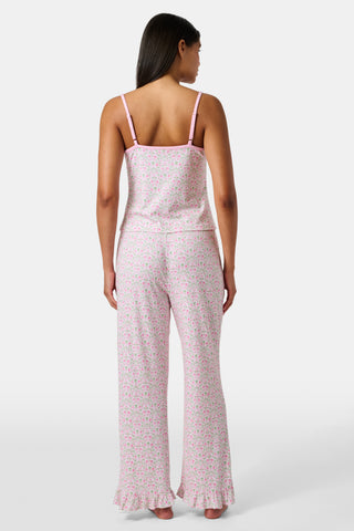 The Garden Gate Floral Lily Set by Roller Rabbit features a pink and white women's loungewear set with a sleeveless, V-neck camisole and loose pants. Made from soft Pima cotton, both pieces showcase a delicate floral pattern and light pink trim. The comfy tank and pants include a drawstring waist and ruffled hems for added comfort and style.