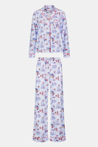 A young child with curly hair stands barefoot against a plain white background, wearing Roller Rabbit’s Kids London Monkey Pajamas—light blue long-sleeve pajamas adorned with playful, colorful patterns featuring guards, clocks, and iconic British landmarks.