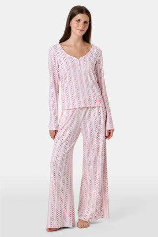A woman smiles while wearing the Roller Rabbit Daisy Heart Stripe Jessie Long Sleeve Tee, a soft Pima cotton top adorned with pink and red daisies, paired with matching pajama bottoms, against a plain white background.