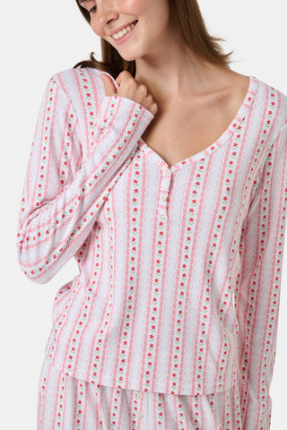 A woman smiles while wearing the Roller Rabbit Daisy Heart Stripe Jessie Long Sleeve Tee, a soft Pima cotton top adorned with pink and red daisies, paired with matching pajama bottoms, against a plain white background.