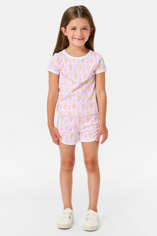 A young girl with long brown hair wears the Roller Rabbit Kids Monkey Playa Play Set and white shoes, standing and smiling against a plain white background.