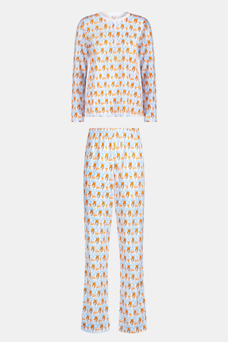 A woman stands barefoot against a plain white background wearing SERFLEX’s Tennessee Lovely Monkey Pajamas: a matching white women’s set with an all-over orange and brown monkey print, featuring long sleeves and full-length pants.