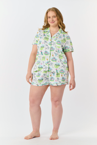 The Roller Rabbit Game, Set, Monkey Polo Pajamas is a two-piece set featuring a short-sleeve button-up shirt and matching shorts. Crafted from soft Pima Cotton, the white fabric is adorned with a playful cartoon animal and house print in green, blue, and yellow tones.