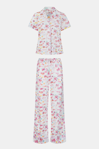 A woman with curly hair models the Roller Rabbit Summer Memories Fiora Pajamas, a Pima cotton set with a colorful sushi print, including a short-sleeve button-up top and long pants, against a white background.