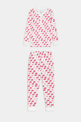 A young child with long brown hair stands barefoot, smiling and wearing the Roller Rabbit Kids Moby Pajamas made from soft Pima cotton, featuring a pink and red mitten pattern, against a plain light background.