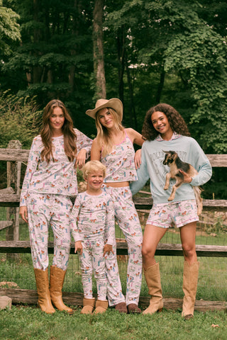 The Saddle Up Joanie Pajamas by Roller Rabbit feature a white sleeveless top and long pants with pink trim. Both pieces are made from soft Pima cotton and decorated with colorful cartoon animal and house prints scattered across the fabric.