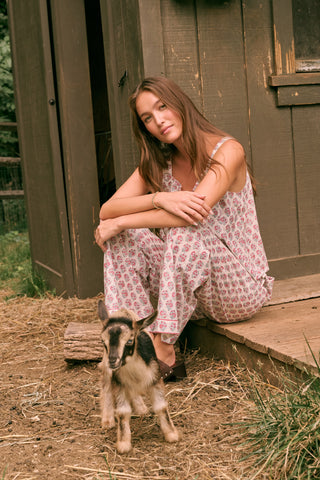Wearing the Roller Rabbit Harvest Floral Benson Set and brown shoes, a woman stands outside a wooden building, looking to her left. She is on a dirt ground, surrounded by greenery and a fence in the background.