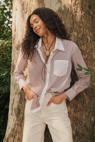 A woman wearing the Roller Rabbit Yarn Dye Stripe Emory Dress—a cotton button-down style with a tie belt and white collar—smiles while looking to the side and pairs the dress with knee-high boots. The background is plain light gray.