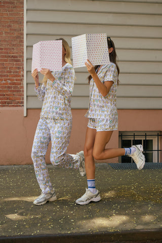 The Roller Rabbit Kappa Alpha Theta Monkey Pajamas set features a white, long-sleeved buttoned top and matching pants, both adorned with a vibrant all-over cartoon print of playful animal characters, including cheerful monkeys.