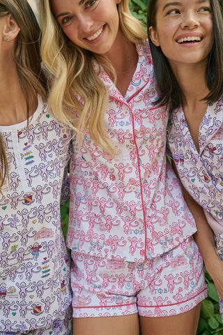 Introducing the Roller Rabbit Gamma Phi Beta Monkey Polo Pajamas: a short-sleeve Pima cotton set featuring a button-up top and matching shorts, adorned with a whimsical pink and blue monkey pattern and red trim on a crisp white background.