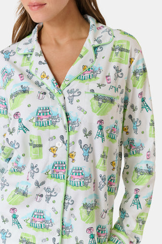 Introducing the Game, Set, Monkey Long Sleeve Polo Pajamas by Roller Rabbit—a cozy white pajama set expertly crafted from soft Pima Cotton. The set features a playful Game Set Monkey print with vibrant green, blue, and yellow animal and nature illustrations. Designed with long sleeves, a button-up polo top, and comfortable drawstring waist pants, this delightful set is showcased against a plain light background.