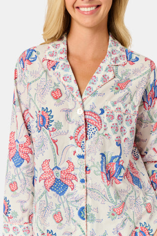 A woman stands against a plain white background, smiling slightly as she models the Amanda Leila Set from Roller Rabbit—a vintage-inspired cotton loungewear ensemble featuring a long-sleeve, button-up pajama top and matching shorts adorned with a colorful floral pattern.