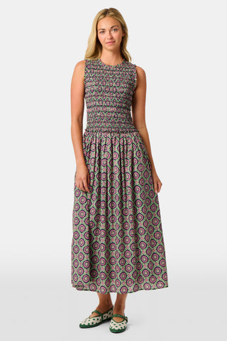 A woman wearing the Roller Rabbit Amelia Emma Dress, featuring a smocked bodice and maxi skirt, stands against a plain white background, paired with green polka-dot flats.
