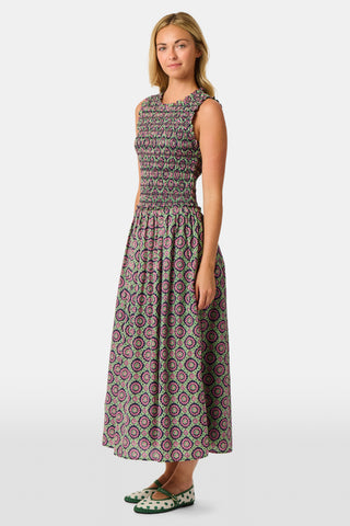 A woman wearing the Roller Rabbit Amelia Emma Dress, featuring a smocked bodice and maxi skirt, stands against a plain white background, paired with green polka-dot flats.