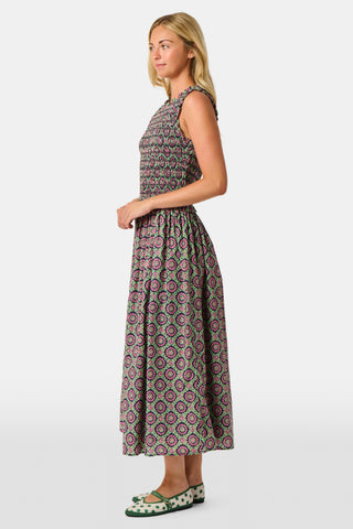 A woman wearing the Roller Rabbit Amelia Emma Dress, featuring a smocked bodice and maxi skirt, stands against a plain white background, paired with green polka-dot flats.