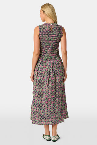 A woman wearing the Roller Rabbit Amelia Emma Dress, featuring a smocked bodice and maxi skirt, stands against a plain white background, paired with green polka-dot flats.