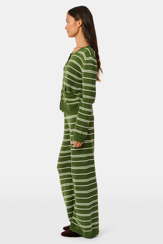 A person wearing the Roller Rabbit Autumn Stripe Olivia Pant—green and white striped, pull-on, flared—and a matching sweater lifts the hem to reveal their midriff. Brown slippers are visible. The background is white.