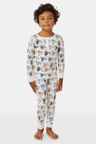 A smiling child in Roller Rabbit’s Kids Boo Crew Pajamas, crafted from soft Pima cotton, sits with arms raised on outdoor steps among women in coordinating patterned pajamas, all sharing a cheerful and relaxed moment together.