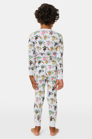 A smiling child in Roller Rabbit’s Kids Boo Crew Pajamas, crafted from soft Pima cotton, sits with arms raised on outdoor steps among women in coordinating patterned pajamas, all sharing a cheerful and relaxed moment together.