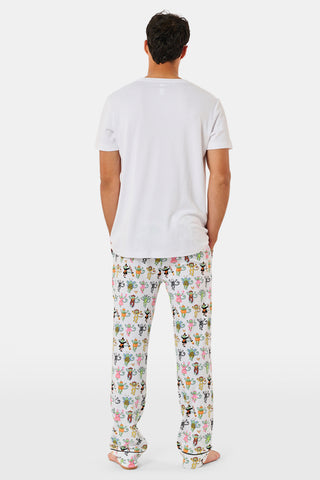 A person stands barefoot against a plain white background, wearing white Roller Rabbit Mens Boo Crew Simon Pants featuring colorful cartoon character prints. The shirt is slightly lifted, revealing the soft Pima cotton waistband.