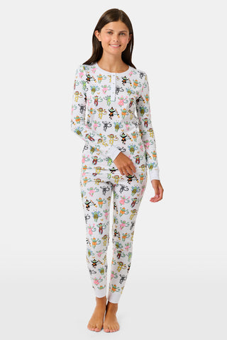 A smiling child in Roller Rabbit’s Kids Boo Crew Pajamas, crafted from soft Pima cotton, sits with arms raised on outdoor steps among women in coordinating patterned pajamas, all sharing a cheerful and relaxed moment together.
