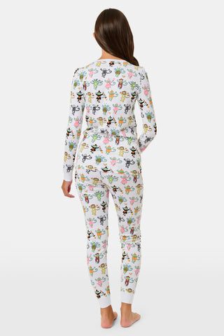 A smiling child in Roller Rabbit’s Kids Boo Crew Pajamas, crafted from soft Pima cotton, sits with arms raised on outdoor steps among women in coordinating patterned pajamas, all sharing a cheerful and relaxed moment together.
