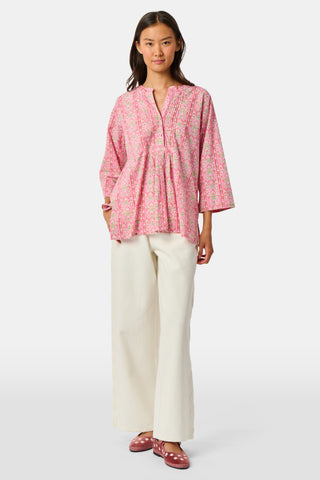 A woman wearing the Roller Rabbit Cora Floral Stripe Pippa Dress—a pink, short-sleeve, midi-length cotton dress with ruffled shoulders and a floral pattern—stands facing forward against a plain white background.