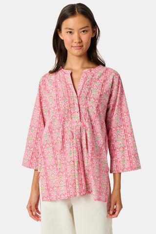 A woman wearing the Roller Rabbit Cora Floral Stripe Pippa Dress—a pink, short-sleeve, midi-length cotton dress with ruffled shoulders and a floral pattern—stands facing forward against a plain white background.