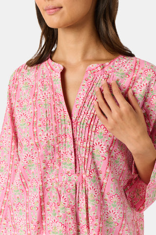 A woman wearing the Roller Rabbit Cora Floral Stripe Pippa Dress—a pink, short-sleeve, midi-length cotton dress with ruffled shoulders and a floral pattern—stands facing forward against a plain white background.