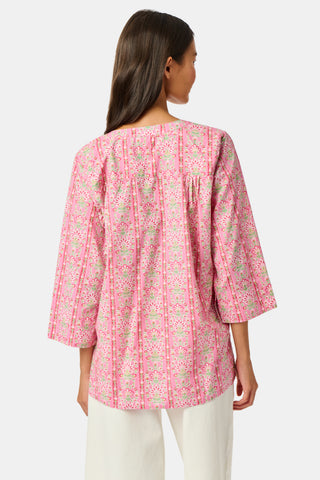 A woman wearing the Roller Rabbit Cora Floral Stripe Pippa Dress—a pink, short-sleeve, midi-length cotton dress with ruffled shoulders and a floral pattern—stands facing forward against a plain white background.