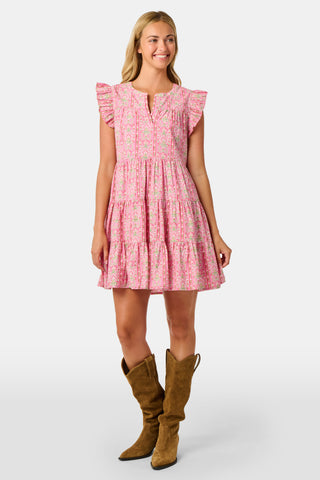 A woman wearing the Roller Rabbit Cora Floral Stripe Pippa Dress—a pink, short-sleeve, midi-length cotton dress with ruffled shoulders and a floral pattern—stands facing forward against a plain white background.