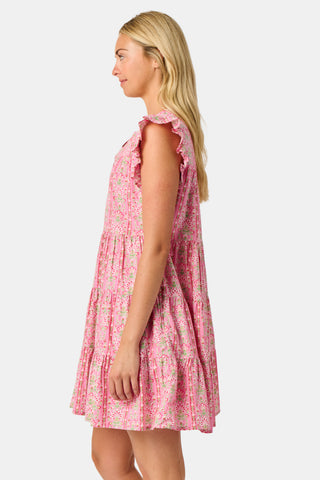 A woman wearing the Roller Rabbit Cora Floral Stripe Pippa Dress—a pink, short-sleeve, midi-length cotton dress with ruffled shoulders and a floral pattern—stands facing forward against a plain white background.