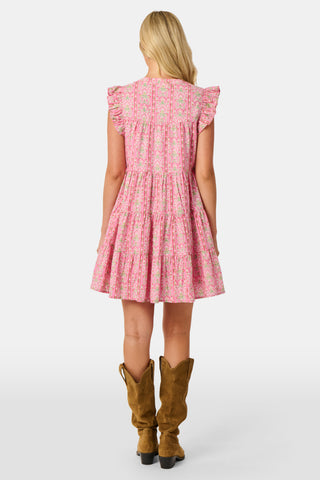 A woman wearing the Roller Rabbit Cora Floral Stripe Pippa Dress—a pink, short-sleeve, midi-length cotton dress with ruffled shoulders and a floral pattern—stands facing forward against a plain white background.