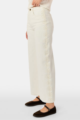 Wearing Roller Rabbit’s Elsa Eyelet Danielle Jean—a high-waisted, wide-leg style in ecru with delicate scalloped lace trim along the sides—paired with a white top and black Mary Jane shoes, the individual stands against a plain white background.