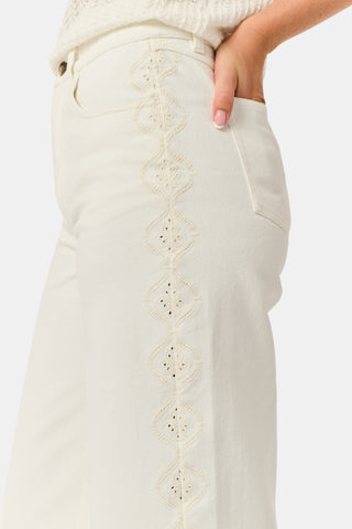 Wearing Roller Rabbit’s Elsa Eyelet Danielle Jean—a high-waisted, wide-leg style in ecru with delicate scalloped lace trim along the sides—paired with a white top and black Mary Jane shoes, the individual stands against a plain white background.