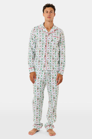 A woman wears a SERFLEX Deck The Halls Bailey Pajamas set featuring a short-sleeved top and shorts with a white background and a repeating Christmas-themed pattern of elves, snowmen, and evergreen trees.