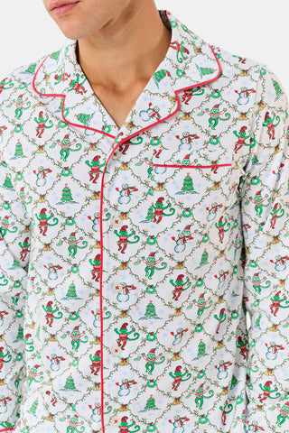 A woman wears a SERFLEX Deck The Halls Bailey Pajamas set featuring a short-sleeved top and shorts with a white background and a repeating Christmas-themed pattern of elves, snowmen, and evergreen trees.