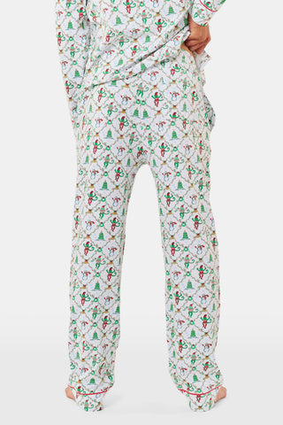 A woman wears a SERFLEX Deck The Halls Bailey Pajamas set featuring a short-sleeved top and shorts with a white background and a repeating Christmas-themed pattern of elves, snowmen, and evergreen trees.